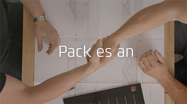 Still of the bkw film showing a topshot of two men shaking hands at a table with blueprints of a building on it with a white text overlay saying "Pack es an".
