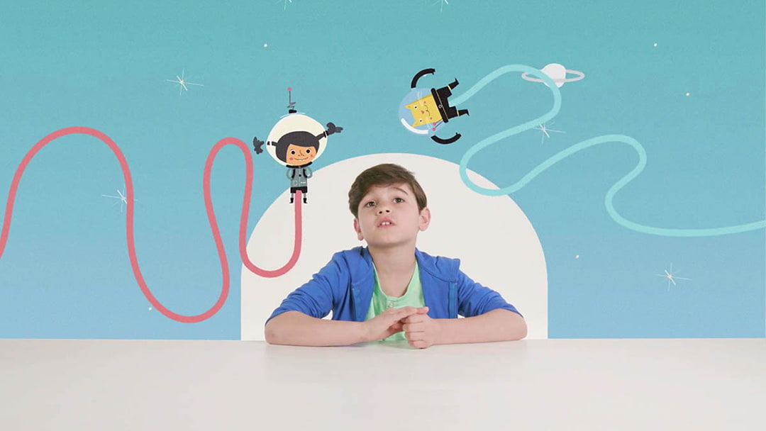 Still of the ubs film showing a boy sitting at a table in front of a blue background with 2D animations of astronauts flying around him.