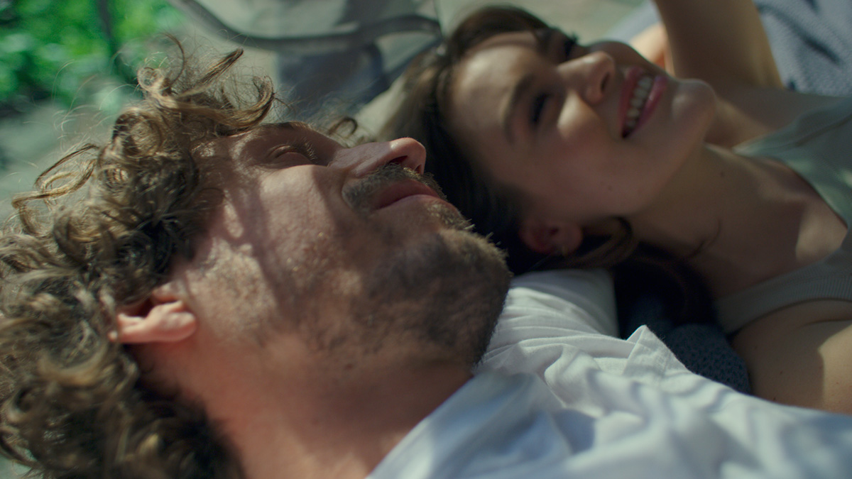 Still of the hüsler nest film showing the faces of a happy couple lying in bed together in the sunlight.